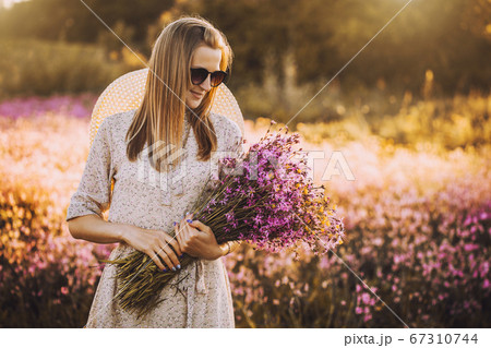 Young woman with a bouquet of wildflowers standing on a sunny blooming meadow Young woman with a bouquet of wildflowers standing on a sunny blooming meadow 67310744
