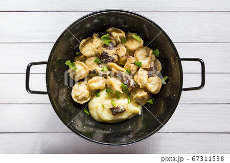 Russian food pelmeni, meat dumplings with mushroom sauce and mashed potatoes in black bowl. Close-up, top view. 67311538