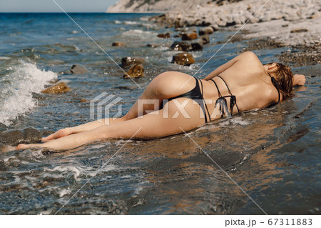 Sexy young woman in bikini posing at stone beach. Attractive model with sporty body 67311883