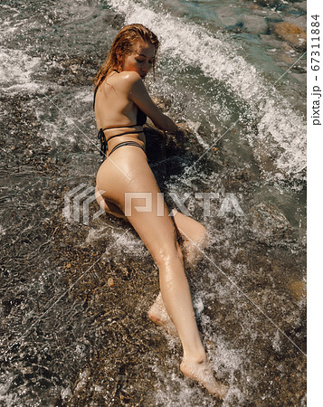 Sexy young woman in bikini posing at stone beach. Attractive model with sporty body 67311884