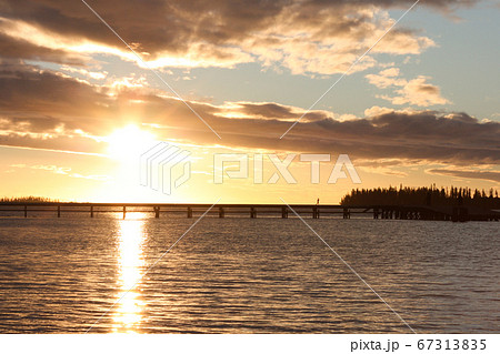 夕日を背景に島に続く橋をジョギングして渡る女性の写真素材