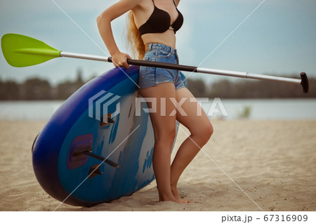 Young attractive woman standing next to paddle board, SUP. Active life, sport, leisure activity concept Young attractive woman standing next to paddle board, SUP. Active life, sport, leisure activity concept 67316909