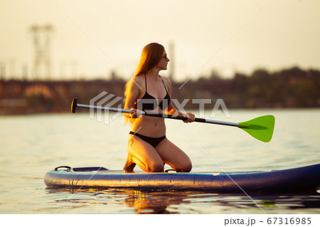 Young attractive woman sitting on paddle board, SUP. Active life, sport, leisure activity concept Young attractive woman sitting on paddle board, SUP. Active life, sport, leisure activity concept 67316985