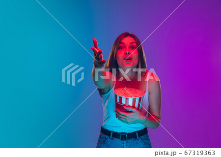 Caucasian young woman's portrait isolated on gradient purple-blue background in neon light, cinema, movie watching Caucasian young woman's portrait isolated on gradient purple-blue background in neon light, cinema, movie watching 67319363
