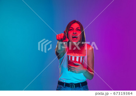 Caucasian young woman's portrait isolated on gradient purple-blue background in neon light, cinema, movie watching Caucasian young woman's portrait isolated on gradient purple-blue background in neon light, cinema, movie watching 67319364
