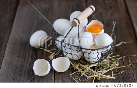 Fresh organic white eggs with eggshell and yolk in metal mesh basket on straw and wooden background	 67320307