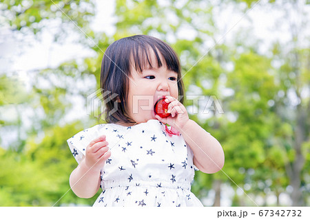 新緑の木々を背景にイチゴを頬張る幼い女の子の写真素材