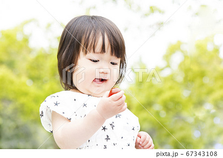 新緑の木々を背景にミニトマトを食べる幼い女の子 67343108