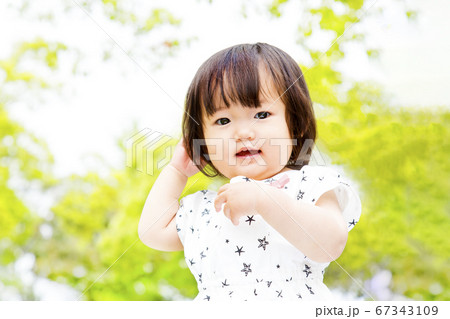 新緑の木々を背景に笑顔で踊る幼い女の子 67343109