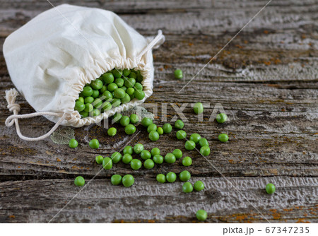 Fresh raw green peas spilling out of eco bag on rustic wooden table	 67347235