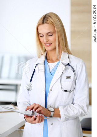 Doctor woman at work in hospital excited and happy of her profession. Blonde physician controls medication history records and exam results while using tablet computer. Medicine and healthcare concept 67350084