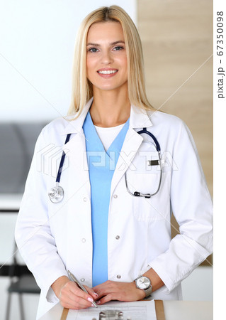 Doctor woman at work in hospital excited and happy of her profession. Blonde physician controls medication history records and exam results while using clipboard. Medicine and healthcare concept 67350098