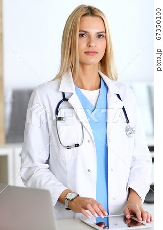 Doctor woman at work in hospital excited and happy of her profession. Blonde physician controls medication history records and exam results while using tablet computer. Medicine and healthcare concept 67350100