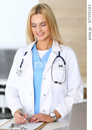 Doctor woman at work in hospital excited and happy of her profession. Blonde physician controls medication history records and exam results. Medicine and healthcare concept 67350103