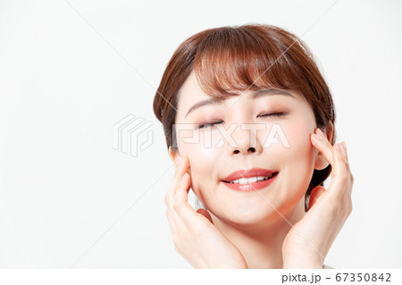 頬に手を当て目を閉じ微笑む20代女性（美容イメージ） 67350842
