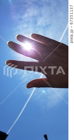 青空と飛行機雲と太陽にかざす手 67351137