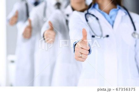 Group of modern doctors standing as a team with thumbs up in hospital office. Physicians ready to examine and help patients. Medical help, insurance in health care, best desease treatment and medicine Group of modern doctors standing as a team with thumbs up in hospital office. Physicians ready to examine and help patients. Medical help, insurance in health care, best desease treatment and medicine 67356375