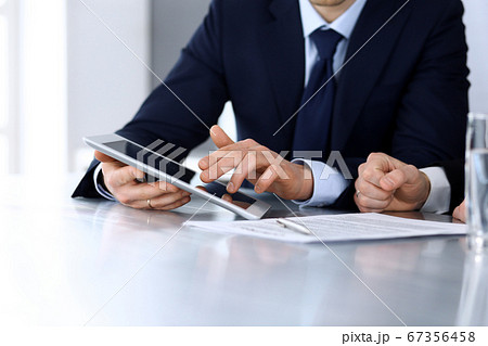 Business people using tablet computer while working together at the desk in modern office. Unknown businessman or male entrepreneur with colleague at workplace. Teamwork and partnership concept Business people using tablet computer while working together at the desk in modern office. Unknown businessman or male entrepreneur with colleague at workplace. Teamwork and partnership concept 67356458