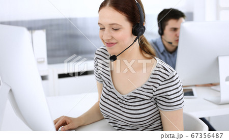 Group of operators at work. Call center. Focus on beautiful woman receptionist in headset at customer service. Business concept and casual striped clothing style 67356487