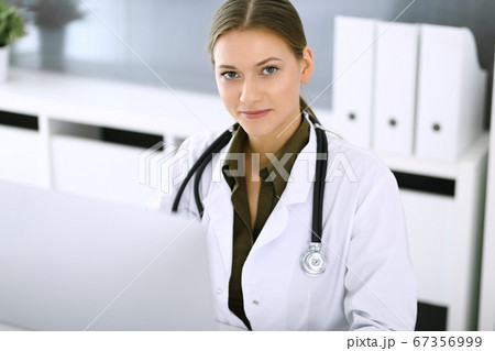 Doctor typing on pc computer while sitting at the desk in hospital office. Physician woman at work. Data in medicine and healthcare Doctor typing on pc computer while sitting at the desk in hospital office. Physician woman at work. Data in medicine and healthcare 67356999