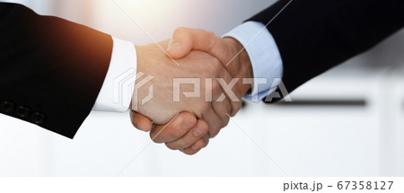 Business people shaking hands after contract signing while standing in sunny office. Teamwork and handshake concept 67358127