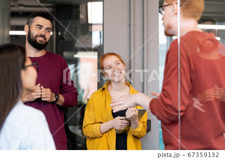 Young cheerful managers in casualwear listening to their colleague explanations Young cheerful managers in casualwear listening to their colleague explanations 67359132