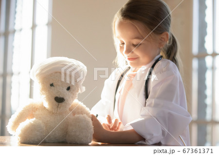 Close up cute little girl pretending doctor vaccinating toy bear 67361371