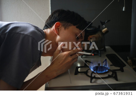 ガスコンロでタバコに火をつける男性 67361931