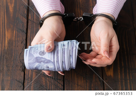 female hands in handcuffs hold twisted money on a dark wooden background female hands in handcuffs hold twisted money on a dark wooden background 67365353
