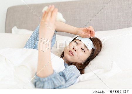 発熱してベッドの中で体温を測る若い女性 67365437