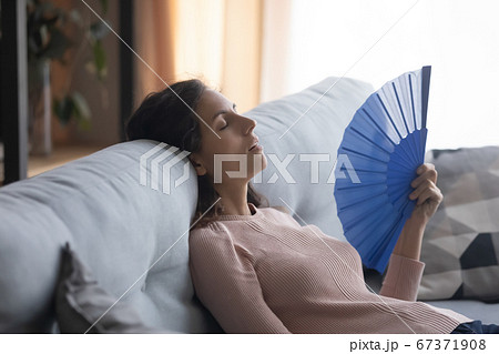 Overheated young woman waving with hand fan at home 67371908