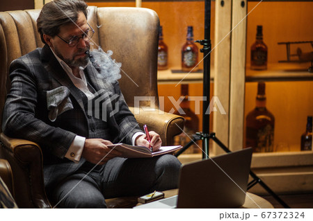 Creative editor pondering over new article, sitting with laptop, smoking pipe 67372324