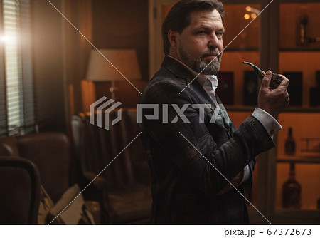 Reflective well-dressed mature bearded man in glasses smoking tobacco pipe Reflective well-dressed mature bearded man in glasses smoking tobacco pipe 67372673
