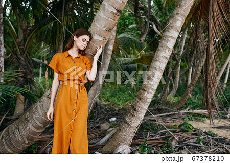 Young woman in a sundress touches a trunk of a palm tree on a nature  67378210