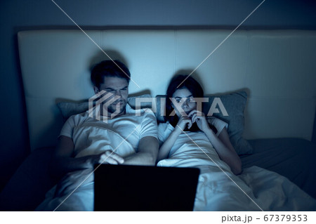 A man and a woman watching movies at night in bed A man and a woman watching movies at night in bed 67379353