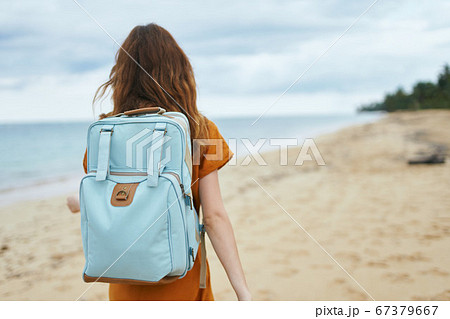 A woman in a yellow dress with a backpack on her back on the shore  67379667
