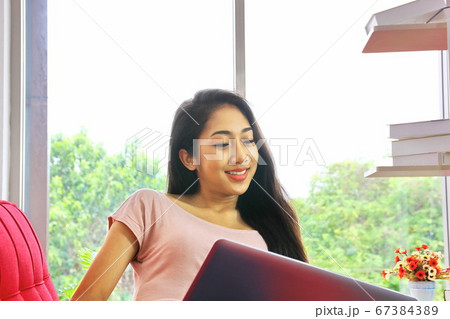 Asian young woman sitting on red sofa using laptop 67384389