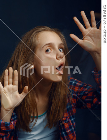 Little girl makes face leaning against the glass 67389381