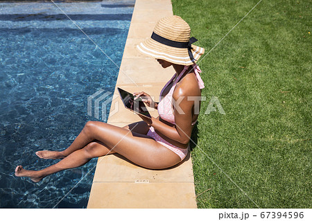 Woman using digital tablet while sitting by the pool 67394596