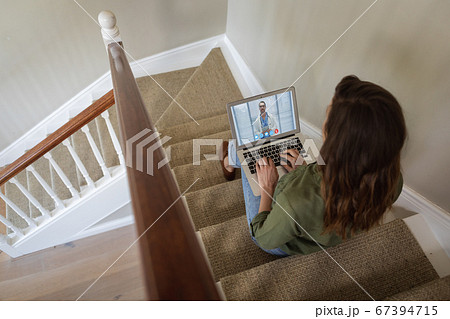 Woman having a video meeting on her laptop while sitting on staircase Woman having a video meeting on her laptop while sitting on staircase 67394715