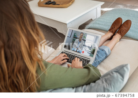 Portrait of woman having a video meeting on her laptop while sitting on couch 67394758