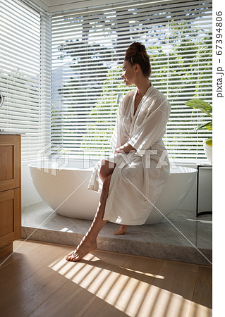 Woman in bathrobe sitting on bathtub Woman in bathrobe sitting on bathtub 67394806