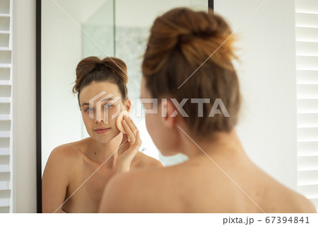 Woman applying makeup to her face while looking in the mirror 67394841