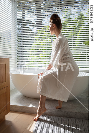 Woman in bathrobe sitting on bathtub 67394855