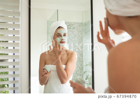 Woman applying face pack while looking in the mirror 67394870