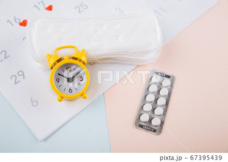 Menstrual calendar with pads, alarm clock and contraceptive pills. Menstruation period concept. Pain reliever for menstrual pain Menstrual calendar with pads, alarm clock and contraceptive pills. Menstruation period concept. Pain reliever for menstrual pain 67395439
