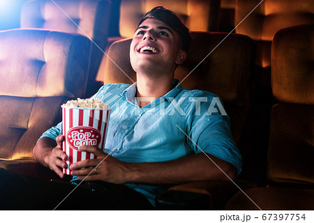 A young man smiling enjoying watching a movie A young man smiling enjoying watching a movie 67397754