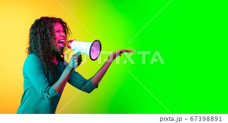 African-american young woman's portrait isolated on gradient yellow-green background in neon light 67398891