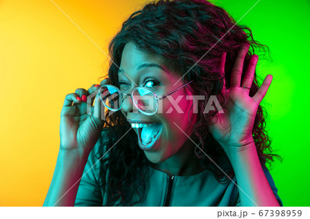 African-american young woman's portrait isolated on gradient yellow-green background in neon light 67398959