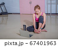 An athletic woman in a sports suit was sitting on the floor with a bottle of water and used a laptop at the gym. Sports and recreation concepts. 67401963
